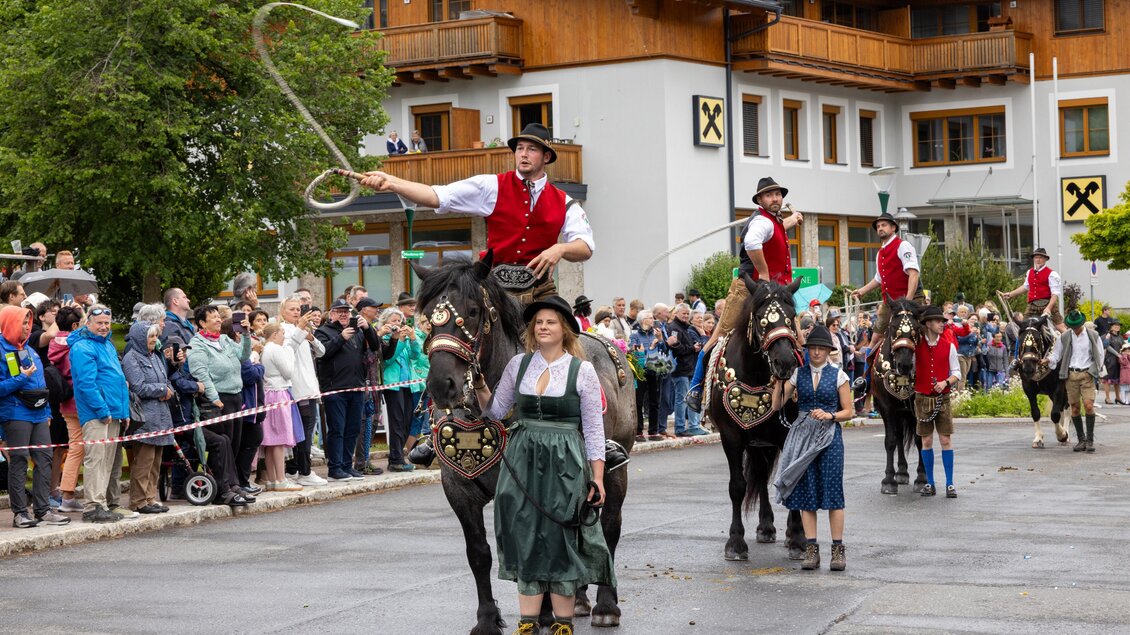 Ein Festumzug mit Reitern in traditioneller Kleidung. Viele Zuschauer stehen an der Straße und beobachten die Veranstaltung.