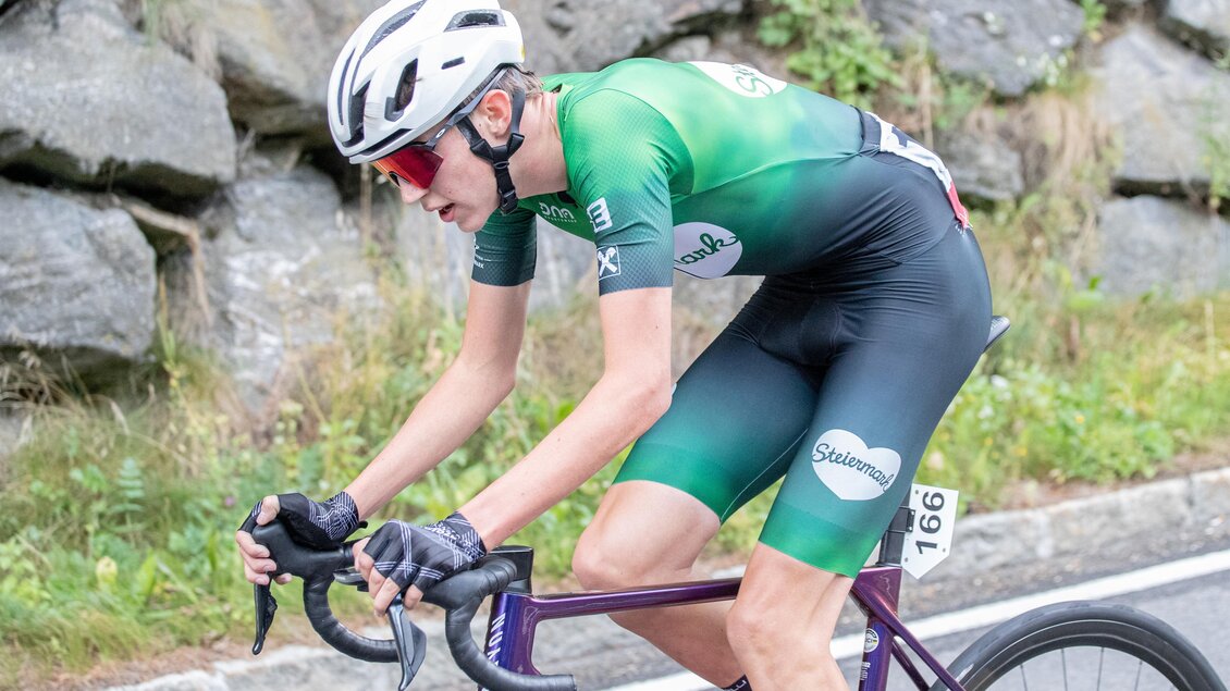 Ein junger Radfahrer in einem grünen Trikot fährt auf einer Straße. Im Hintergrund sind Steine und etwas Vegetation zu sehen. | © Oststeiermark Tourismus
