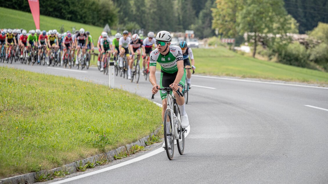 Eine Gruppe von Radfahrern fährt eine kurvenreiche Straße entlang. Im Vordergrund ist ein einzelner Radfahrer in einem grünen Trikot zu sehen. | © Oststeiermark Tourismus