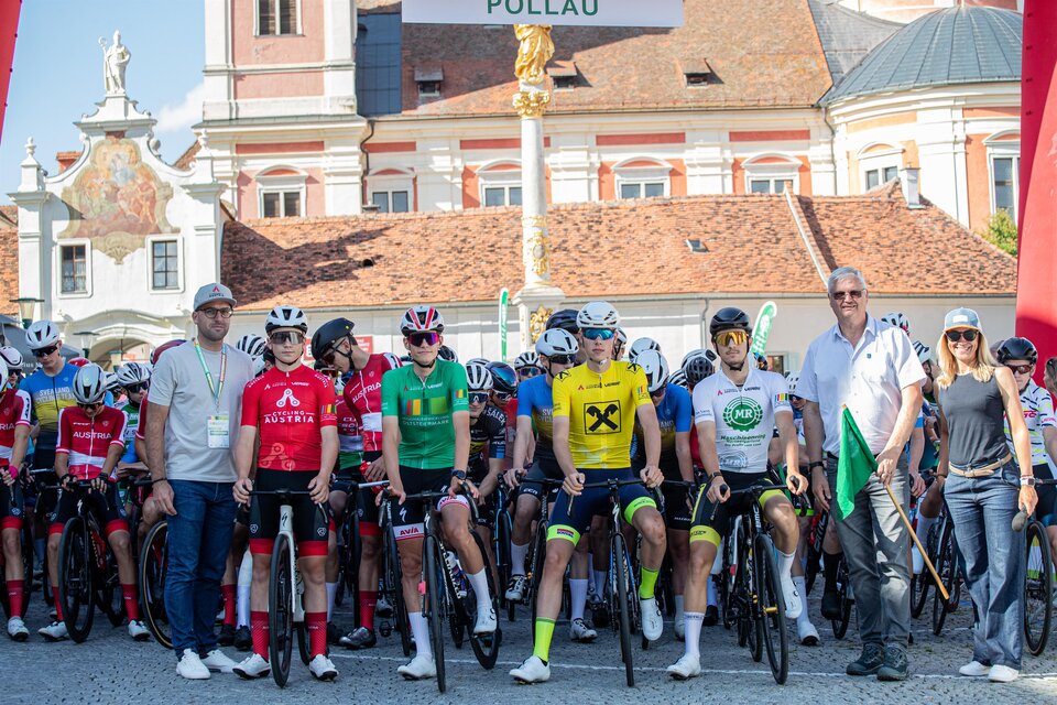 Eine Gruppe von Radfahrern steht an der Startlinie eines Rennens in Pollau. Im Hintergrund sind historische Gebäude und eine festliche Atmosphäre zu sehen. | © Peter Maurer