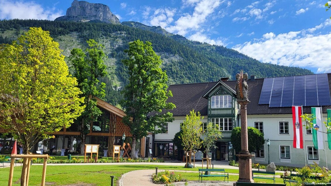 Der Veranstaltungssaal sowie das Kur- und Amtshaus in Altaussee. Im Vordergrund ist der Kurpark mit seinen saftigen Laubäumen und im Hintergrund der Altausseer Hausberg Loser zu sehen.  | © Petra Kirchschlager