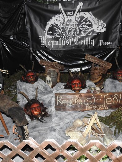 Eine düstere Darstellung mit einer Schaufensterpuppe und roten Masken. Im Hintergrund befindet sich ein schwarzes Banner mit dem Schriftzug „Republis Teitln“. | © Oststeiermark Tourismus