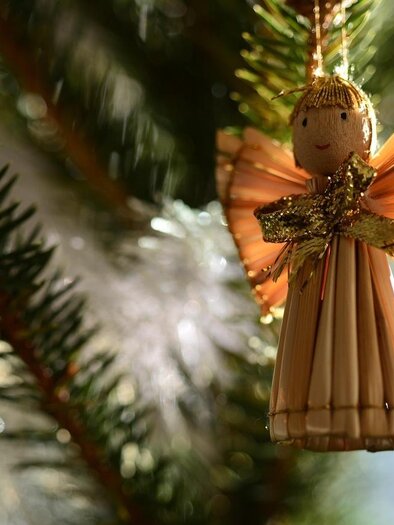 A sweet figure of an angel sits next to a burning candle. The background is gold-colored and sparkles festively. | © Pixabay