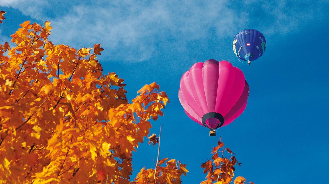 Zwei Heißluftballons schweben über bunten Herbstblättern. Der Himmel ist klar und blau. | © Haring