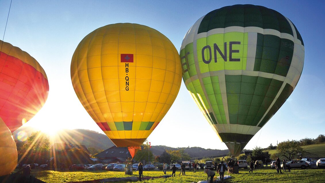 Drei bunte Heißluftballons stehen auf einem Feld. Die Sonne scheint am Himmel und sorgt für eine schöne Atmosphäre. | © Zugschwert