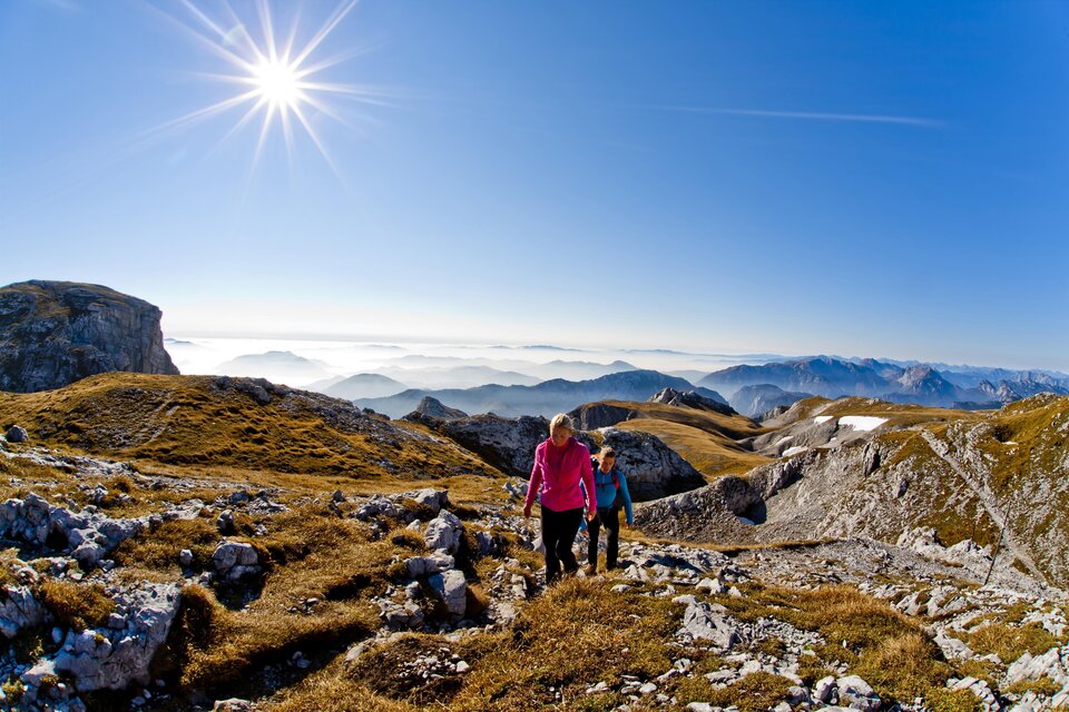 Das Bild zeigt ein Paar beim Wandern auf dem Hochschwab, Blauer Himmel, Sonnenschein und die hügelige Landschaft