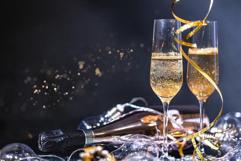 Zwei Sektgläser mit sprudelndem Champagner stehen auf einem Tisch. Um sie herum sind Luftschlangen und Glanzlichter zu sehen, die eine festliche Stimmung erzeugen. | © Pixabay.com