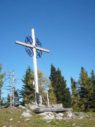 A large wooden cross stands on a hill, surrounded by trees. The sky is clear and blue. | © Irmgard Totz