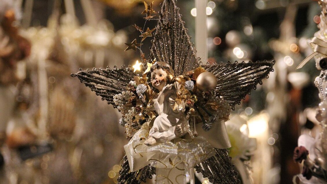 Ein glitzernder Weihnachtsstern mit einer kleinen Engelfigur in der Mitte. Der Stern ist mit vielen Farben und festlichen Dekorationen geschmückt.