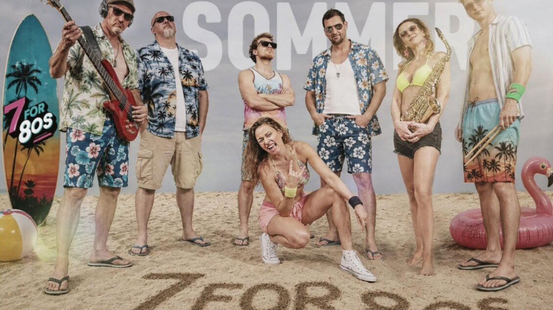 <p>Die Band 7 for 80s posiert am Strand mit ihren Instrumenten. Im Hintergrund sind Strandutensilien und der Schriftzug "SOMMER" zu sehen.</p> | © Inez Grieshofer