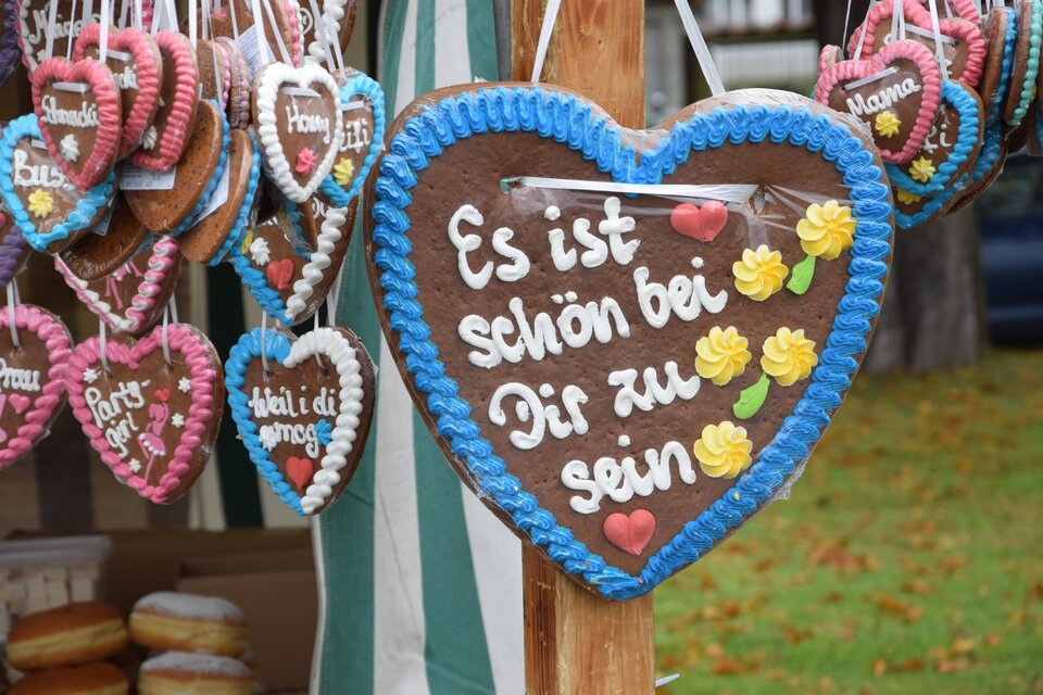 Ein herzförmiges Lebkuchen-Schild mit der Aufschrift "Es ist schön bei Dir zu sein" und bunten Verzierungen. Im Hintergrund hängen weitere süße Herzschilder. | © Marktgmeinde Niklasdorf