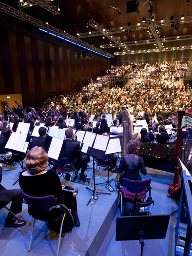 An orchestra is playing in front of a large audience in a modern concert hall. The musicians are sitting on stage and focusing on their instruments. | © Graz Tourismus-Harry Schiffer