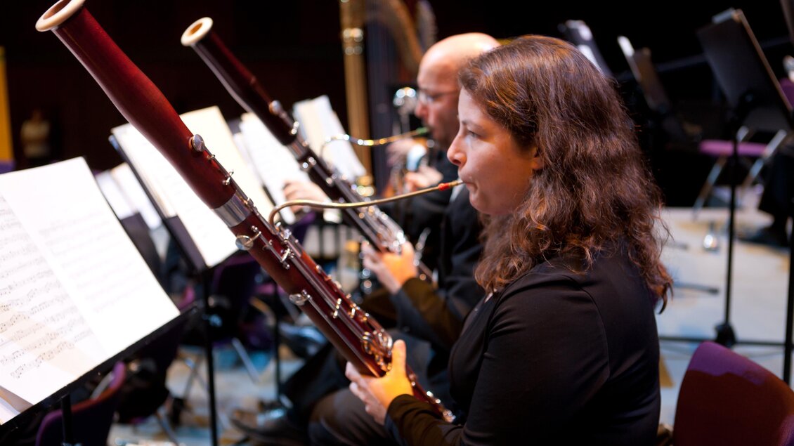 Ein Musiker spielt Fagott auf der Bühne während eines Orchestermusikauftritts. Im Hintergrund sind Notenblätter und weitere Instrumente zu sehen. | © Graz Tourismus-Harry Schiffer