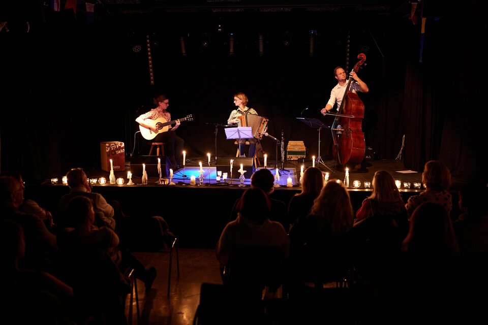 Ein intimes Konzert mit drei Musikern auf der Bühne, umgeben von Kerzenlicht. Das Publikum sitzt aufmerksam und genießt die Atmosphäre. | © Bernd Wimmer