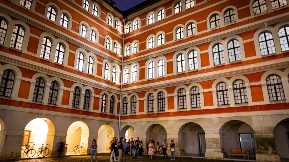 Ein historisches Gebäude mit vielen Fenstern und bunten Fassaden. Menschen stehen in einem Innenhof und genießen den Abend. | © Graz Tourismus - Werner Krug