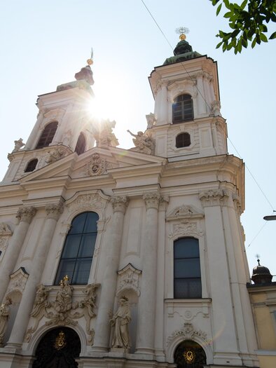 Eine beeindruckende Kirche mit zwei Türmen und barocker Architektur. Die Sonne scheint hell darüber und verleiht der Szene eine besondere Atmosphäre. | © graz-tourismus-harry-shiffer