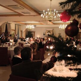 A festively decorated Christmas party in an elegant hall. The guests are seated at tables and enjoy the atmospheric ambiance by candlelight. | © Weinschloss Thaller