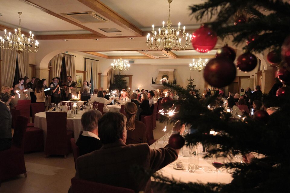Eine festlich dekorierte Weihnachtsfeier in einem eleganten Saal. Die Gäste sitzen an Tischen und genießen die stimmungsvolle Atmosphäre bei Kerzenlicht. | © Weinschloss Thaller
