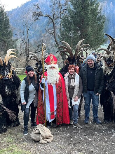 Eine Gruppe von Menschen in traditionellen Kostümen steht im Freien. In der Mitte ist eine Person in einem roten Gewand, umgeben von Figuren mit Hörnern. | © Seeberger Alpakas