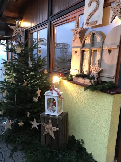 Weihnachtlich geschmückter Eingangsbereich beim Buschenschank Konrad mit Christbaum, leuchtendem Adventfenster und liebevoller Dekoration aus Holz und Naturmaterialien. | © Buschenschank Konrad