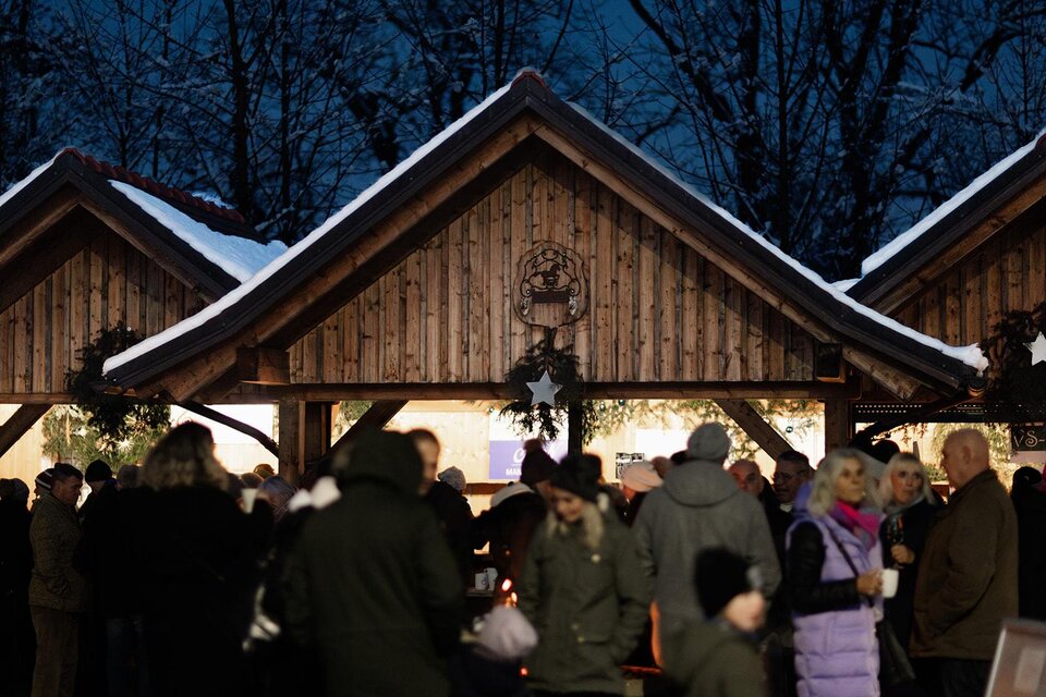 Ein festlicher Weihnachtsmarkt mit beleuchteten Holzständen und vielen Menschen. Die Umgebung ist von winterlicher Atmosphäre und Schnee geprägt. | © Achromatic photography