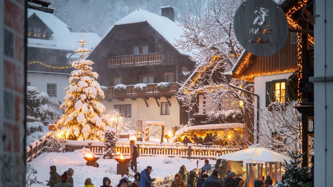 Ein malerisches Dorf im Winter mit schneebedeckten Häusern und einem beleuchteten Weihnachtsbaum. Viele Menschen genießen die festliche Atmosphäre und das winterliche Ambiente. | © Christoph Huber
