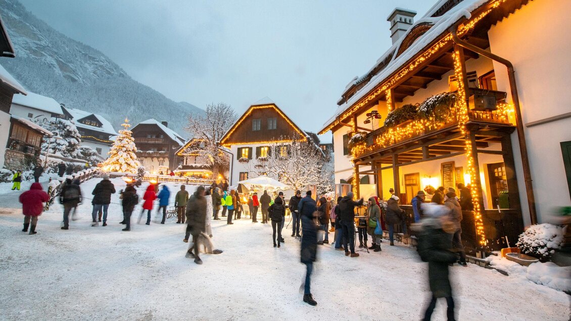 Ein winterliches Dorf mit schneebedeckten Straßen und festlich beleuchteten Häusern. Menschen in warmen Kleidern genießen die weihnachtliche Atmosphäre. | © Christoph Huber