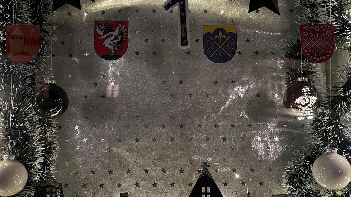Ein dekorativer Adventskalender mit einer stilisierten Stadtsilhouette und Weihnachtsmotiven. Enthält Lichter und verschiedene weihnachtliche Elemente. | © Alexandra Wippel