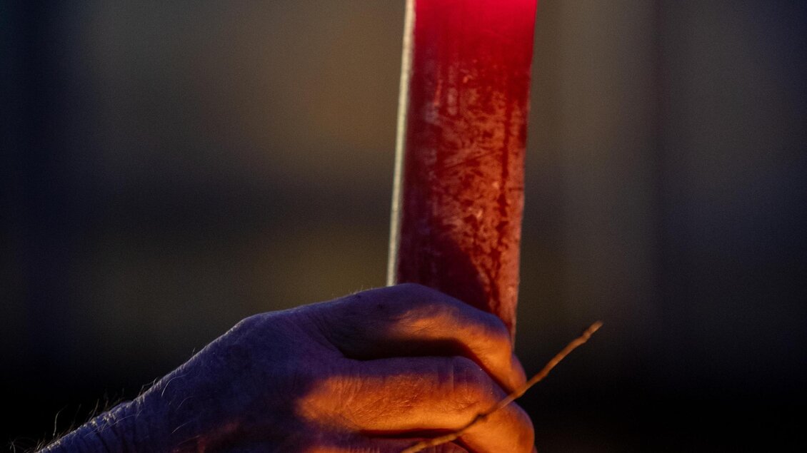 Eine brennende rote Kerze wird von einer Hand gehalten. Der Hintergrund ist dunkel und schaffte eine gemütliche Stimmung. | © Pranzl