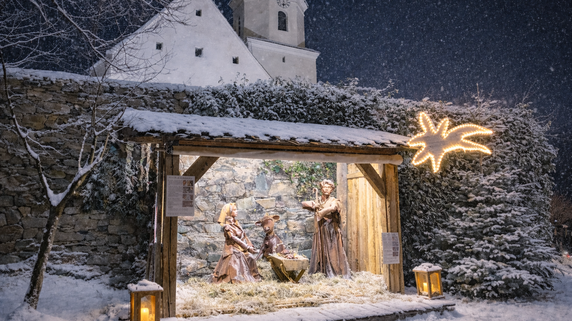 Eine weihnachtliche Szenerie mit einer Krippe, umgeben von Schnee. Im Hintergrund ist eine Kirche sichtbar, und es schneit leicht. | © Oststeiermark Tourismus