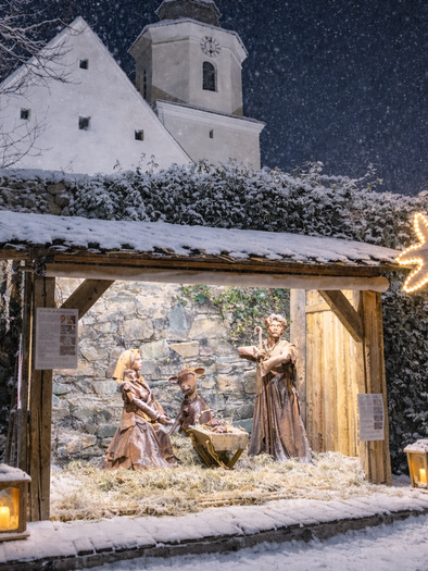 Eine weihnachtliche Szenerie mit einer Krippe, umgeben von Schnee. Im Hintergrund ist eine Kirche sichtbar, und es schneit leicht. | © Oststeiermark Tourismus