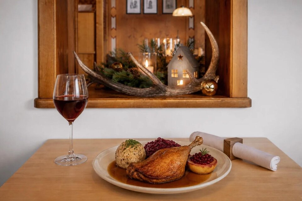 Ein Teller mit einer knusprigen Ente, Semmelknödel und Rotkraut serviert im Gasthaus Seeblick in Grundlsee. Daneben steht ein Glas Rotwein und dahinter schöne Dekoration. | © Karl Steinegger