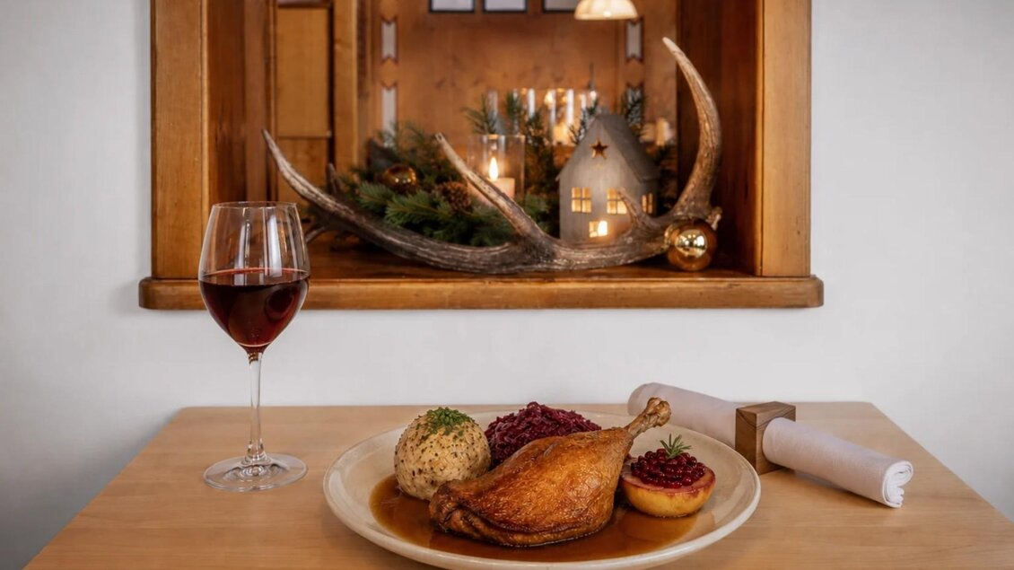 Ein Teller mit einer knusprigen Ente, Semmelknödel und Rotkraut serviert im Gasthaus Seeblick in Grundlsee. Daneben steht ein Glas Rotwein und dahinter schöne Dekoration. | © Karl Steinegger