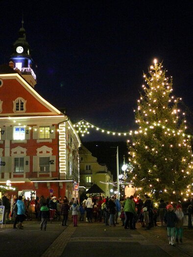A festive cityscape at night with a illuminated Christmas tree. There are many people on the street enjoying the festive atmosphere. | © Gemeinde DL