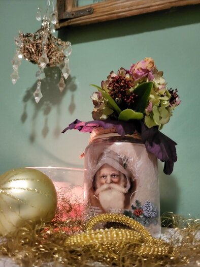 A decorated glass with an image of an old man and colorful flowers. Next to it are golden decorations and a sparkling ball. | © Malermeisterbetrieb Enzi