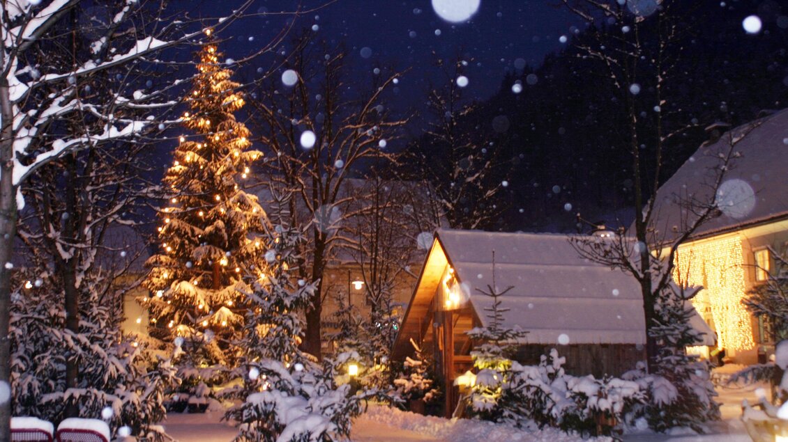 Ein verschneiter Garten bei Nacht mit einem beleuchteten Weihnachtsbaum. Sanfte Schneeflocken fallen auf die winterliche Landschaft. | © Marktgemeinde Passail
