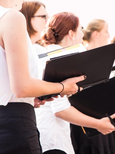 Eine Gruppe von Sängern steht in Schwarzem und Weiß, während sie Notenblätter in der Hand halten. Die Atmosphäre ist konzentriert und musikalisch. | © TV Südsteiermark - Adobe Stock