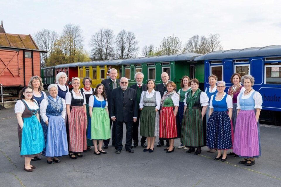Eine Gruppe von Menschen in traditionellen Trachten steht vor bunten Zugwaggons. Die Atmosphäre ist festlich und freundlich. | © StainZeit - Stainzer Chor