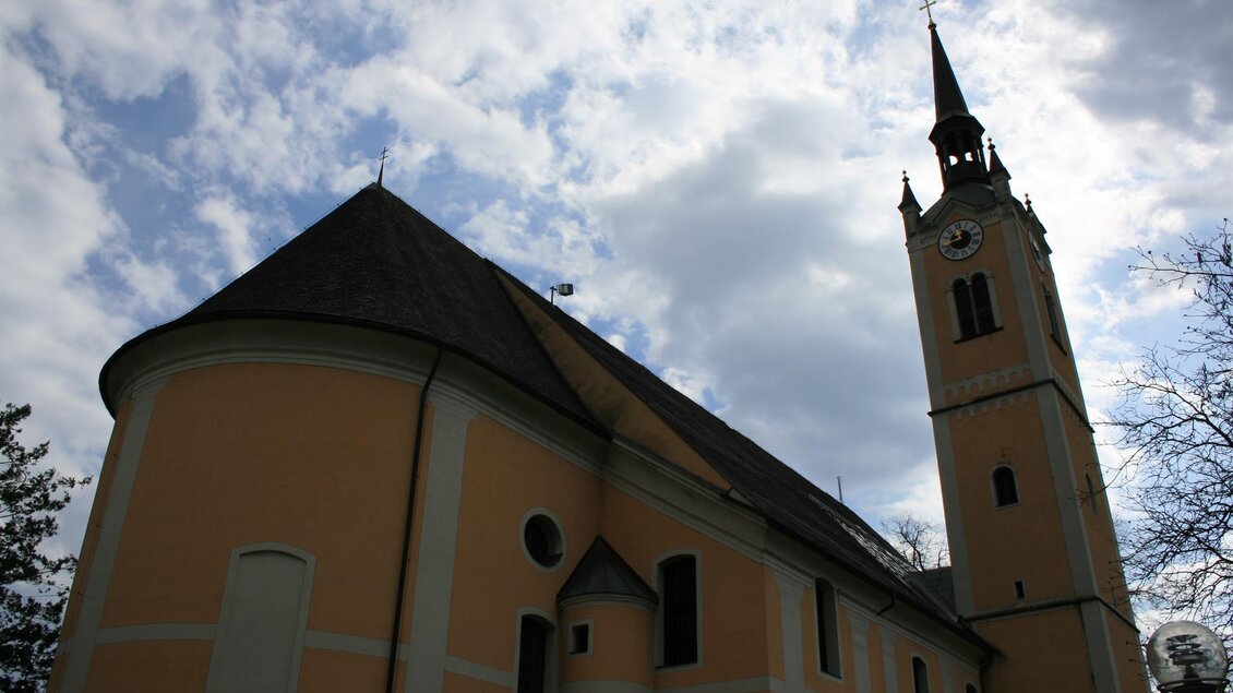 Eine historische Kirche mit einem hohen Turm und einem schönen gelben Anstrich. Der Himmel ist bewölkt, was der Szene eine ruhige Stimmung verleiht.