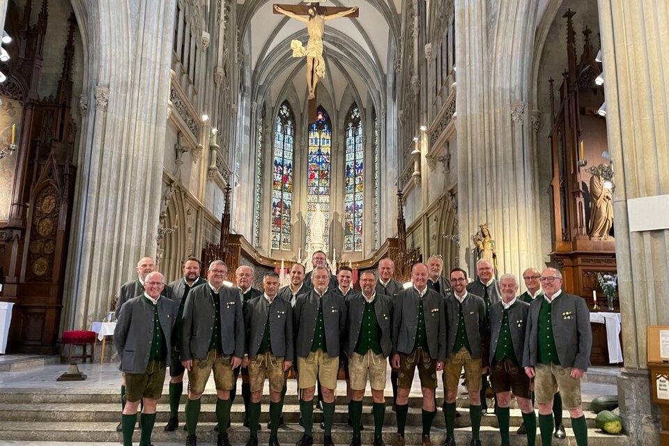 Eine Gruppe von Männern in traditioneller Tracht steht in einer Kirche. Im Hintergrund sind beeindruckende Kirchenfenster und ein Kreuz sichtbar. | © MGV Ehrenhausen