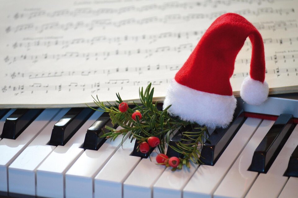 Ein Klavier mit einem Weihnachtsmann-Hut und einem kleinen Zweig mit Beeren. Im Hintergrund sind Notenblätter sichtbar. | © Pixabay