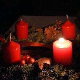 Ein Adventskranz mit roten Kerzen und Weihnachtsdekoration. Die Atmosphäre ist gemütlich und festlich im gedämpften Licht.