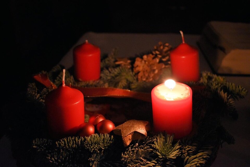 Ein Adventskranz mit roten Kerzen und Weihnachtsdekoration. Die Atmosphäre ist gemütlich und festlich im gedämpften Licht.