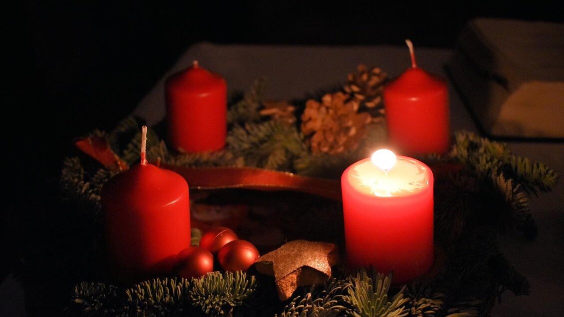 Ein Adventskranz mit roten Kerzen und Weihnachtsdekoration. Die Atmosphäre ist gemütlich und festlich im gedämpften Licht.