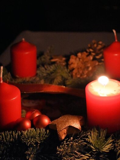 An Advent wreath with red candles and Christmas decorations. The atmosphere is cozy and festive in the dim light.