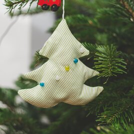 A decorative fabric Christmas tree ornament hangs on a fir tree. The ornament has green and blue accents. | © markus-spiske-unsplash