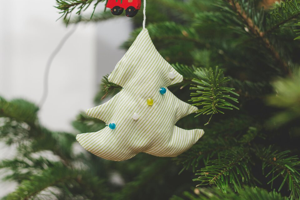 Ein dekorativer Weihnachtsbaum-Anhänger aus Stoff hängt an einem Tannenbaum. Der Anhänger hat grüne und blaue Akzente. | © markus-spiske-unsplash