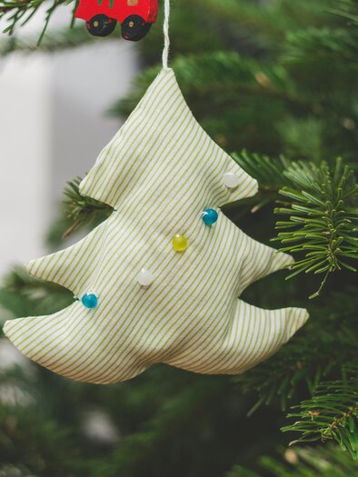 A decorative fabric Christmas tree ornament hangs on a fir tree. The ornament has green and blue accents. | © markus-spiske-unsplash