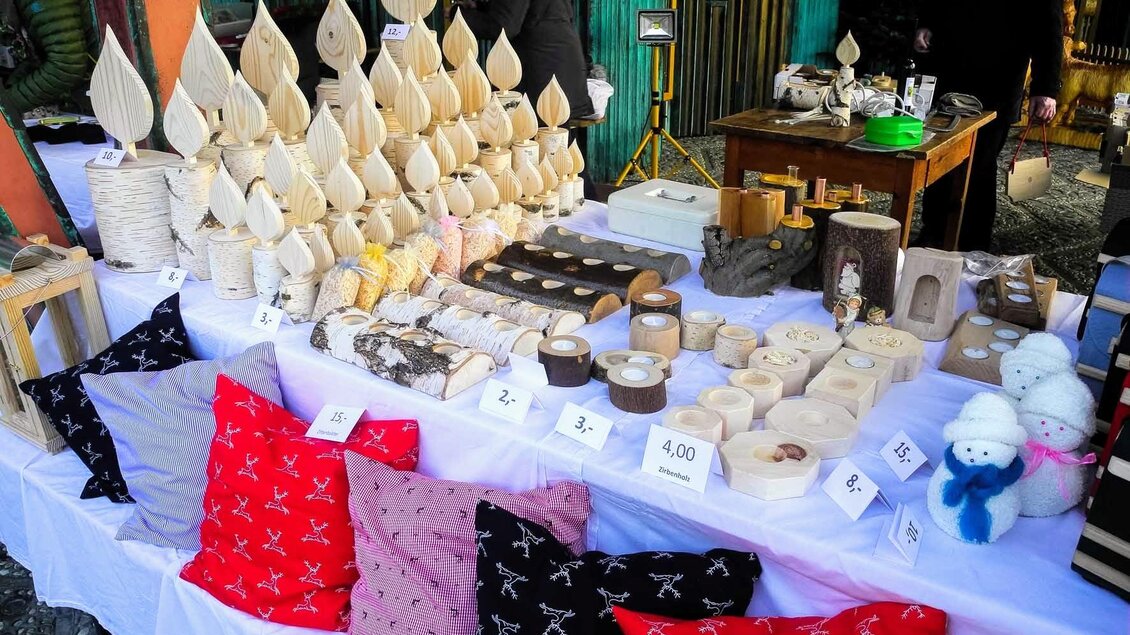 Ein Marktstand mit handgefertigten Holzprodukten und Kissen in bunten Farben. Die Dekoration umfasst verschiedene Formen und Größen, die ansprechend angeordnet sind. | © Helge Hochrinner