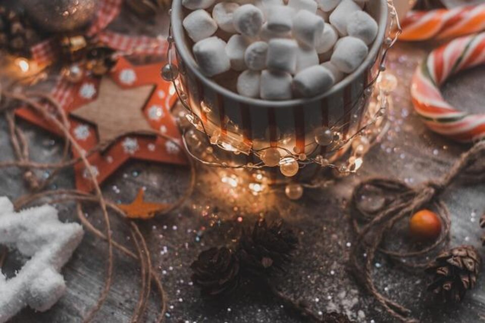 Eine Tasse heiße Schokolade mit kleinen Marshmallows steht auf einem festlich dekorierten Tisch. Um die Tasse sind Lichter und Weihnachtsdekorationen arrangiert. | © Pixabay